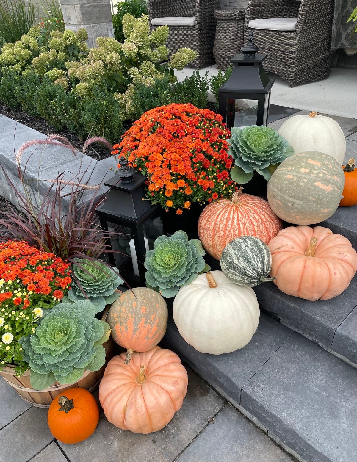 Autumn patio display with orange mums, ornamental cabbage, lanterns, and heirloom pumpkins